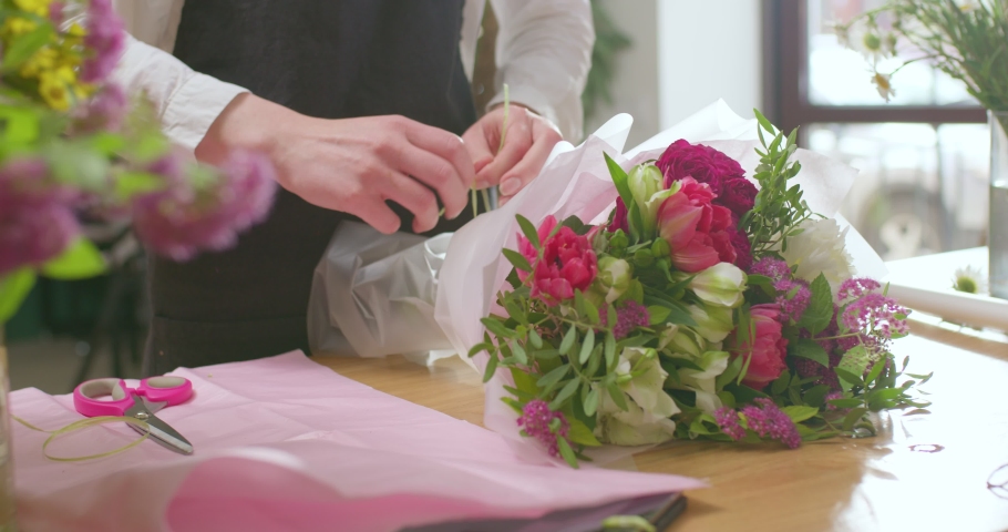 Master class on making bouquets. Talented Woman Finishing Decoration Of Spring bouquet. caucasian woman in black apron arranging, making beautiful bouquets with her own hands, at work. close-up Royalty-Free Stock Footage #1086201233