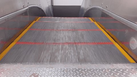 First person view of close up footage of moving empty modern escalator stairs, escalator moves steps up, steps are marked in red and yellow