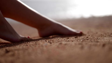 bare feet of young woman on sand, closeup view, moving sensually, ocean shore