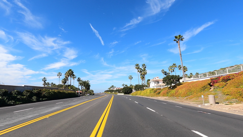 4K HD video driving POV on PCH, Pacific Coast Highway, on the outskirts of Laguna beach with housing then ocean view. Blue cloudy sky. Royalty-Free Stock Footage #1086207011