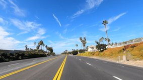 4K HD video driving POV on PCH, Pacific Coast Highway, on the outskirts of Laguna beach with housing then ocean view. Blue cloudy sky.