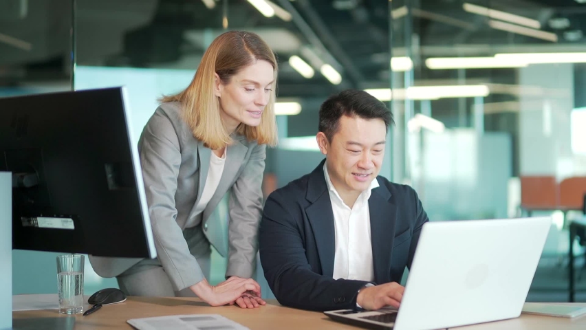 happy coworkers discuss project strategy by looking and pointing at laptop pc computer monitor screen. multiethnic business team in the office. confident mature asian man explaining young female Royalty-Free Stock Footage #1086209765