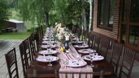 A beautiful outdoor wedding setting in pink flowers. plates and cutlery on a wooden table against a backdrop of greenery. On a Summer day 
a wooden reception table in the backyard, decorated with rose