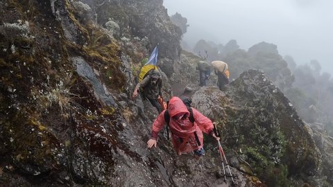 A hiker in a raincoat climbs the dangerous damp rocky stones uphill. Climbing Kilimanjaro, Tanzania, Africa. Rain in the mountains.