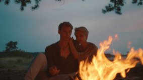 Couple sit next to camp fire, cuddle and have romantic evening in forest. cinematic shot in evening light of dusk of man and woman warm next to campfire. Millennial outdoor lifestyle - Powered by Shutterstock - Get 15% off with code: PIKWIZARD15