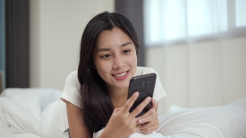 Young beautiful asian woman talking on cell phone, using smart phone on bed to social media at home. Lifestyle of Pretty female using mobile phone to network internet online before sleep.