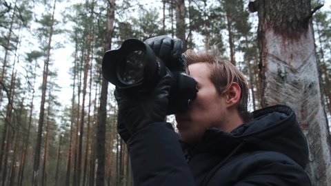 A young blond male photographer takes pictures of nature. Photographer takes pictures in the woods in the winter couple. Young photographer. 
