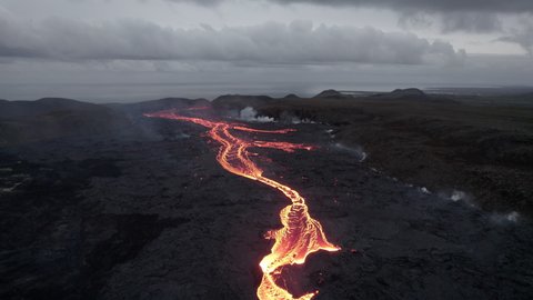 Wide Drone Flight Tilting Down Over Rivers Of Molten Lava Flowing Amongst Volcanic Terrain Of Smoke And Black Rocks, Iceland