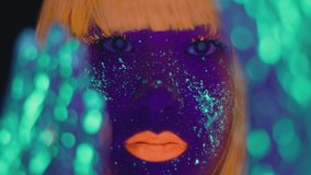 Close up portrait of young woman with bright fluorescent makeup and body art posing to camera, gesturing with glowing hands, selective focus, slow motion