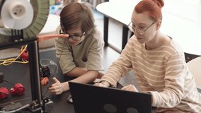 High angle view of Caucasian schoolboy and young female teacher sitting at desk in classroom in front of laptop screen and analyzing program code boy made for his robot - Powered by Shutterstock - Get 15% off with code: PIKWIZARD15
