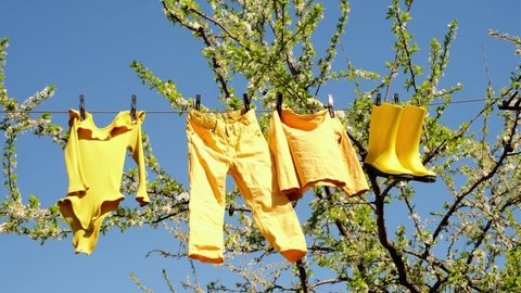 Children's underwear and shoes hang in the garden on a clothesline on a sunny day. Trousers, bodysuits and rubber boots dry on a shoelace