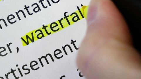 Word waterfall undelnines among other words printed on white paper. Waterfall development concept. Water fall SDLC system development life cycle methodology software, closeup