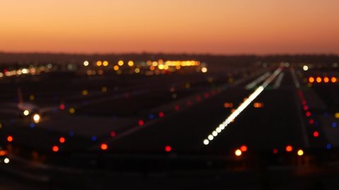 Defocused airport runway lights at night, plane or airplane taking off from airstrip, twilight dusk after sunset. Aircraft or airliner jet departure from aerodrome, San Diego airfield, California USA