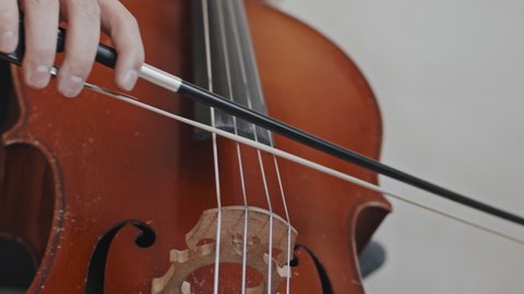 Close-up of unrecognizable musician playing double bass with bow indoors at daytime