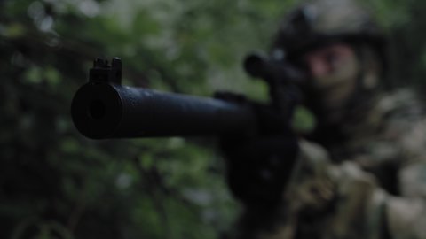 An armed soldier on military operation with rifle in his hands with sniper scope in battle operation through dense forest. SWAT in military ammunition: helmet, camouflage, bulletproof vest and rifle