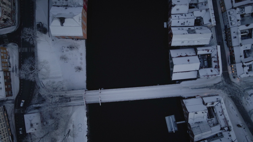 Top View Of Nidelva River And Old Town Bridge In Trondheim, Norway With Snow-covered Houses On The Riverbank At Winter. aerial