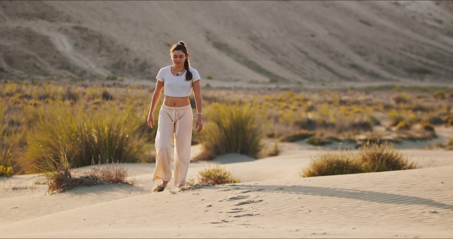 Young brunette yoga instructor walking towards the camera on a sand hill early in the morning