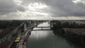 Drone flying over Guadalquivir river with amusement park and ferris wheel on shore, Seville in Spain. Aerial forward