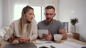 caucasian couple sitting at kitchen table online shopping using digital tablet