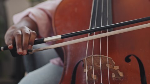 Close-up of cropped unrecognizable musician playing double bass with bow sitting indoors