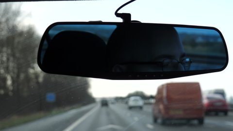 View from inside of car. Driver's face in the rear view mirror and blurred defocused transport on British motorway. Handheld shot keeping horizon level.