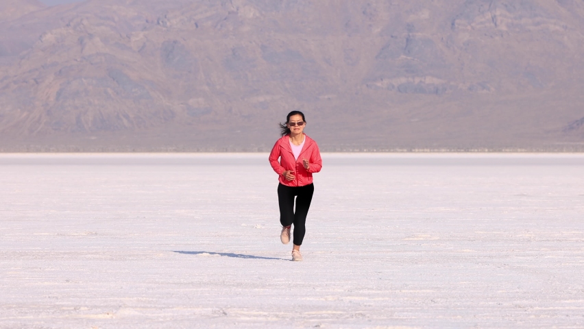 Asian woman jogging across the Bonneville Salt Flats flats in Utah. Slow Motion.