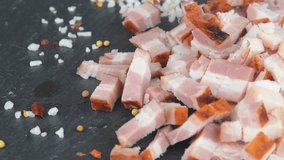 Meat delicacy. Sliced bacon cubes, basil and seasonings on a rotating slate tray. Macro