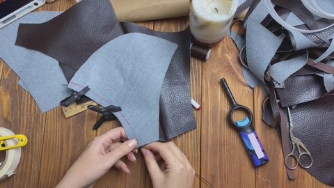 Woman sews eco-leather clothing with thread and needle on wooden table. Workshop of seamstress. Neck corset for cosplay or costume.