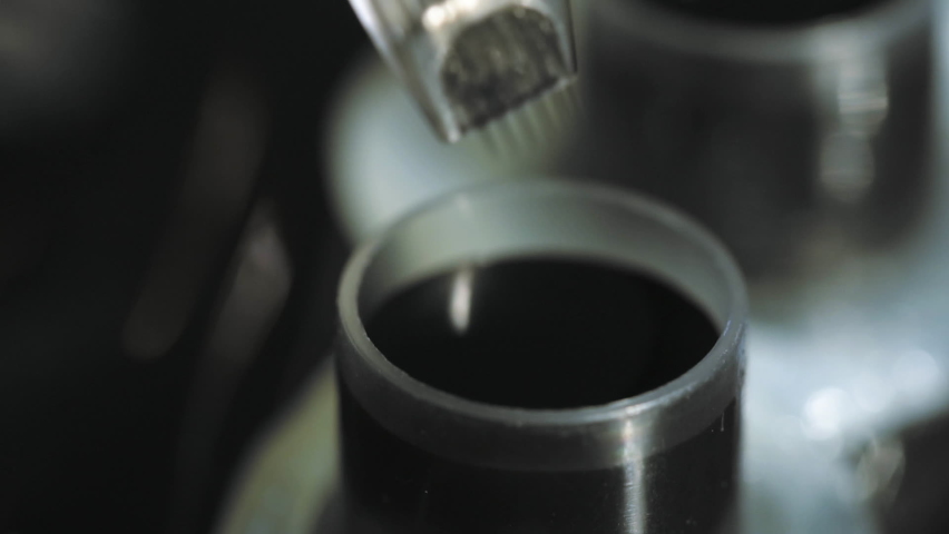 Close-up view of tattoo studio, artist loading magnum needles bar with liquid black color ink from fixed with vaseline cap. Tattooing machine preparation. Dark dye paint fluid filling in tattooist gun