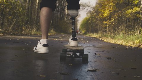 A young man with a metal prosthetic leg rides a skateboard in an autumn park. Go in for sports with an artificial leg. a11y