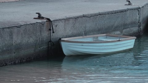 Small wooden white boat stands at the pier in the port. Dark water. Cloudy day at the boathouse. Sea transport. Marina. Small port in a fishing village. Holidays on the coast. Water ripple.