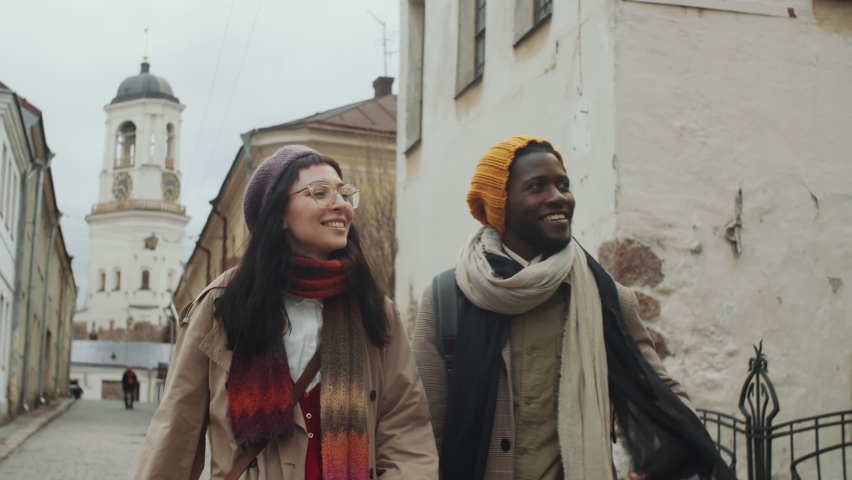 Young multiethnic tourists walking together down the street in old town, pointing at building and discussing architecture