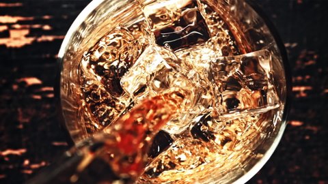 Whiskey is poured into a glass of ice cubes. Against a dark background. Top view. Filmed on a high-speed camera at 1000 fps. High quality FullHD footage