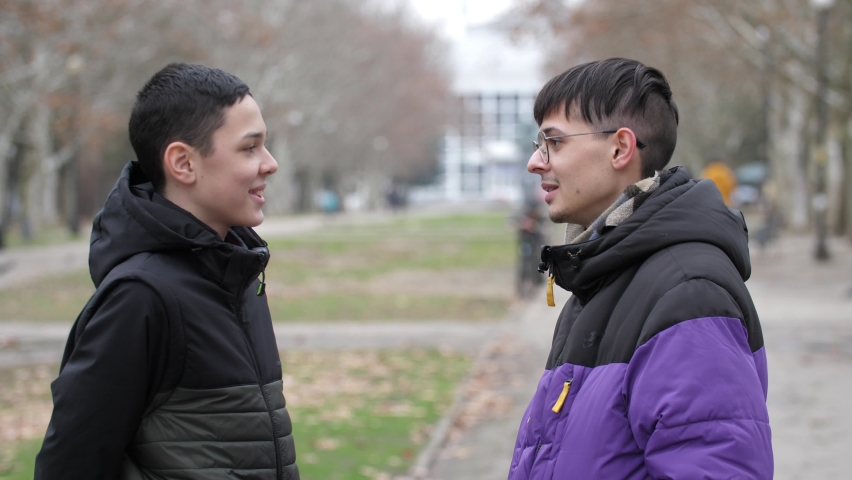 A 13-year-old boy and a young guy are standing on the street, talking and laughing merrily.