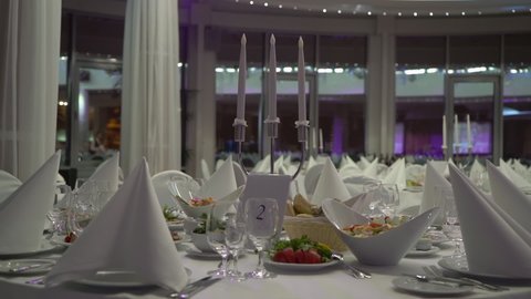 Holiday dinner in restaurant. Decorated hall for reception, celebration party, wedding, anniversary or birthday. White tables with food. Glass and plates, electric candles.