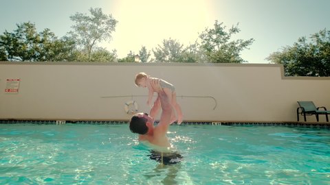 Cute little daughter and his father swimming in the pool. The father is holding his daughter in his hands and embracing. Close up view
