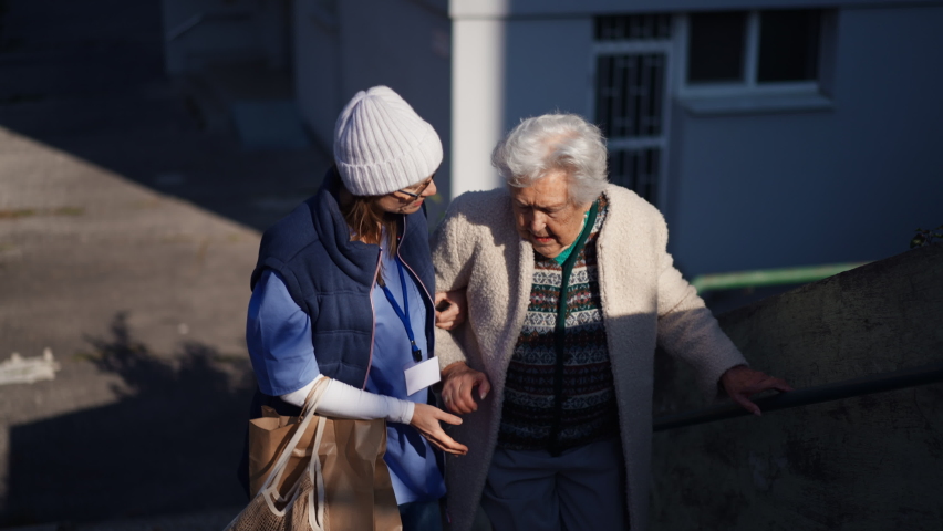 A caregiver helping senior woman to walk up stairs in town in winter. Royalty-Free Stock Footage #1086264227