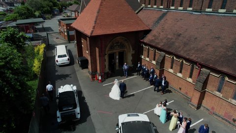 Enfield , United Kingdom (UK) - 01 23 2022: Rising aerial view above wedding bride posing for photographs outside traditional village church