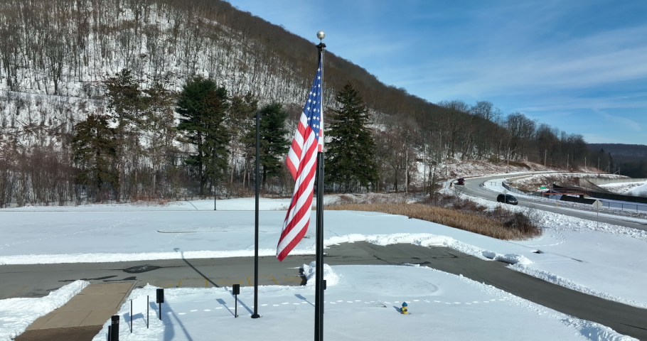 American flag flagpole in cold winter day in snow. Mountain vista. Aerial orbit.
