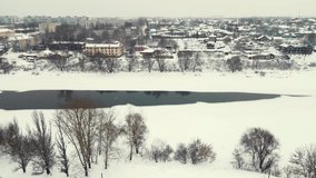 Beautiful winter landscape, aerial view, frozen river and a town on the shore. Everything is covered with white snow, copy space. Screensaver, footage for intro, background, titles. UHD 4K.