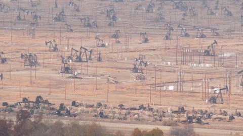 Wells with pump jacks on oil field, California USA. Rigs for crude fossil extraction working on oilfield. Industrial landscape, derricks in desert valley. Many pumpjacks platforms on oilwells pumping.