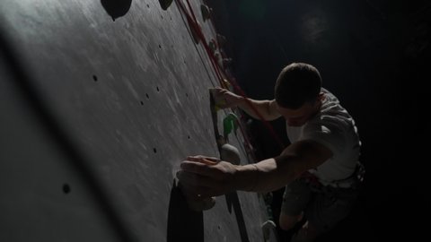 Young climber training on a climbing wall, practicing rock-climbing and moving up, using insurance, cinematic lighting.