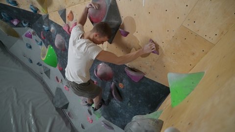 Climber training on a climbing wall, practicing rock-climbing, view from above.