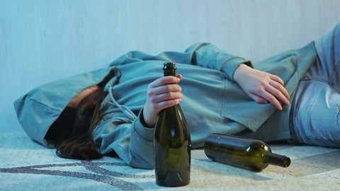 Teenage girl with a bottle of alcohol. Dependent girl alone on the floor in depression. The concept of teenage alcoholism.