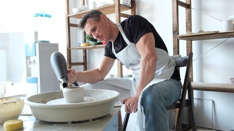 A man dries a white clay product with a hair dryer on a potter's wheel. Craft, creativity, the process of working on a potter's wheel.