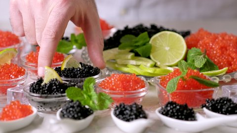 Tasting red salmon caviar and black beluga sturgeon salted roe. Hands pick caviar in bowl. Set of delicious snacks on banquet, close up. Expensive delicacy, serving. Bowls with red and black caviar 