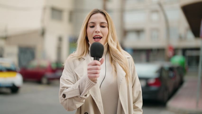 Young blonde woman journalist speaking using microphone at street