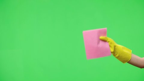 Woman's hand in yellow rubber gloves wipes window glass with dry rag against the background of green screen chroma key. Housewife does housework. Cleaning transparent shiny glass from dust. Close up.