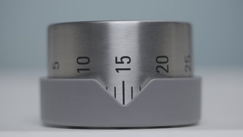 Silver kitchen timer with numbers rotates and counts timelapse. Egg timer, kitchen alarm clock, countdown minutes. Clockwork for time lapse during cooking, close up on a gray background. Slow motion.