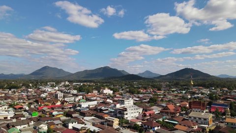 Aerial steady footage of Chiang Khan revealing rooftops and mountains in the horizon with fantastic clouds while the traffic moves on the road, taken from the Walking Street, Loei in Thailand.